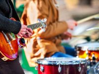 close up of musicians playing electric guitar and drums in an outdoor setting