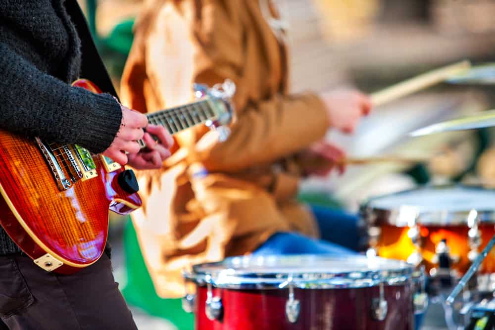 close up of musicians playing electric guitar and drums in an outdoor setting
