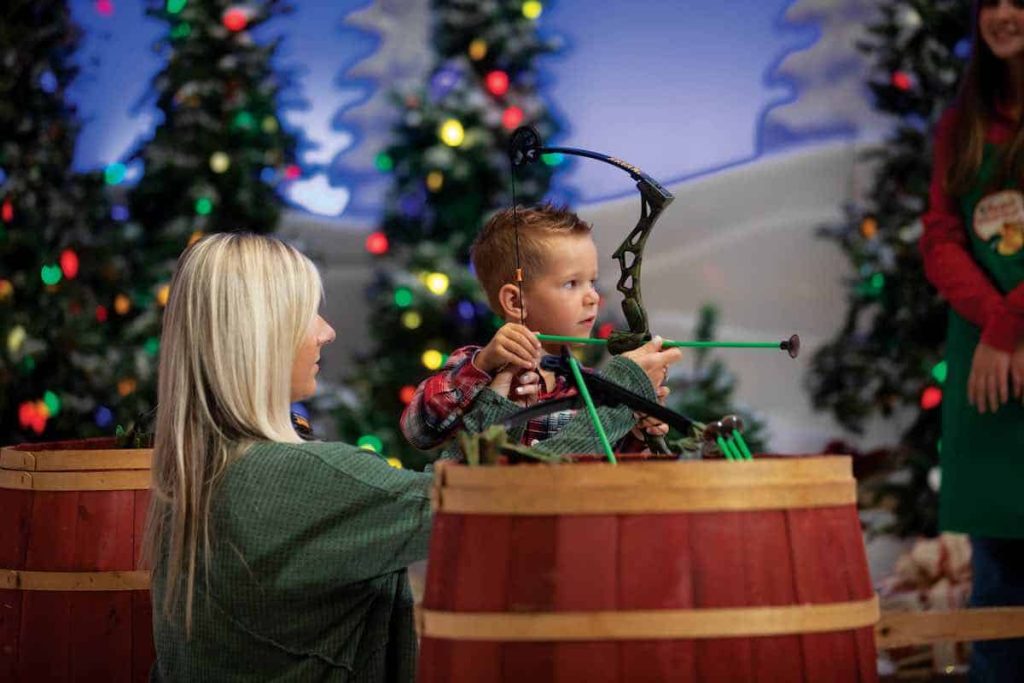 Young boy playing with toy bow and arrow, with decorated Christmas trees in the background
