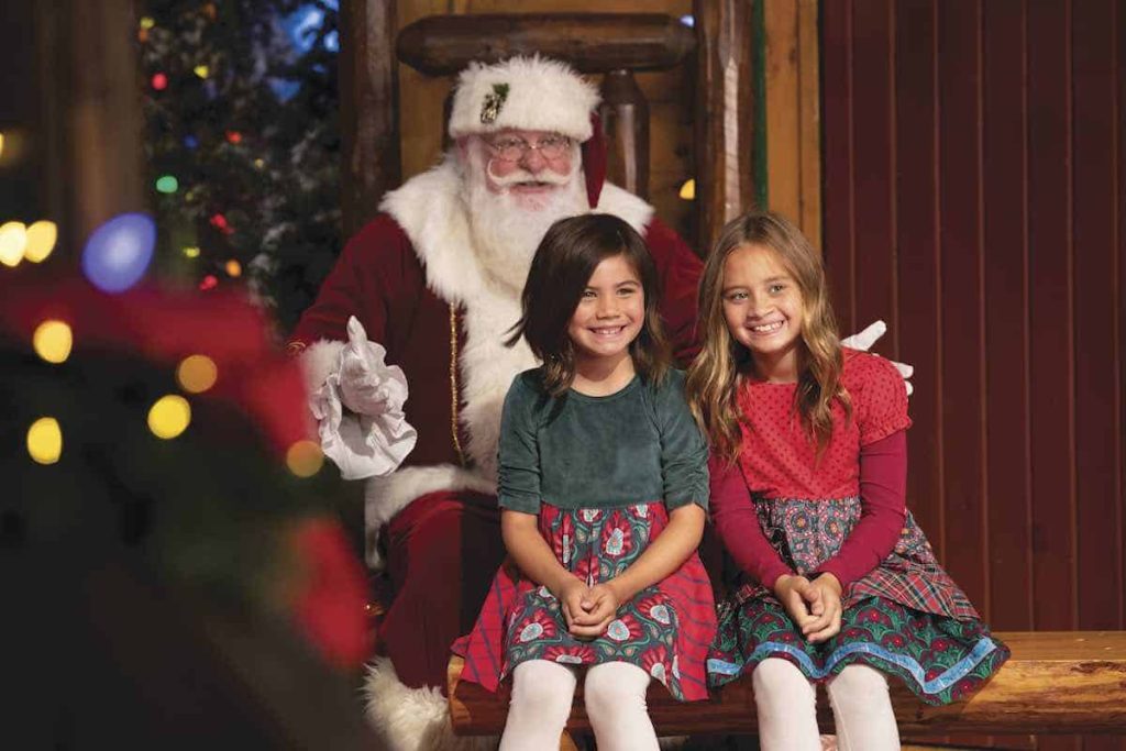 Two girls sitting on bench in front of Santa