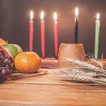 Kwanzaa holiday concept with decorate seven candles red, black and green, gift box, pumpkin,corn and fruit on wooden desk and background.