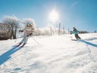 Two Women Skiing Down Beech Mountain Slope with Snowy Trees in Background