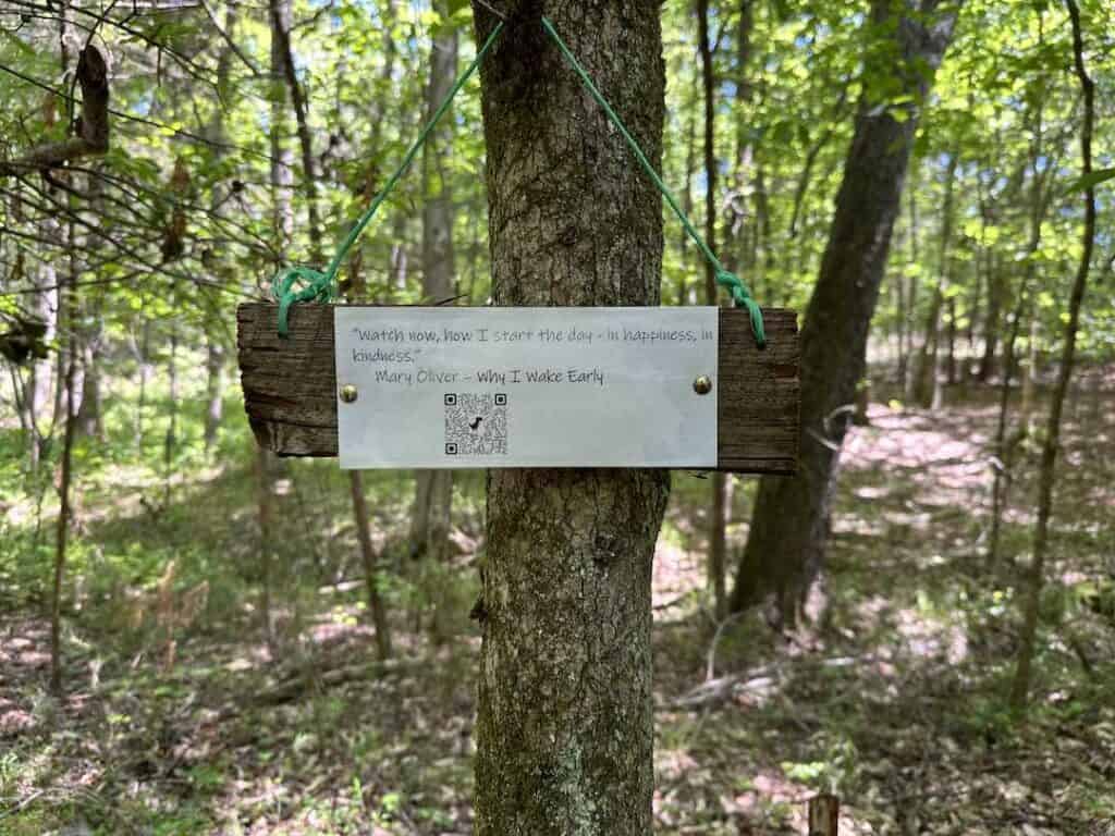 Sign with quote from Mary Oliver and QR code hung from tree
