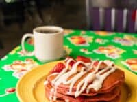 red velvet pancakes topped with strawberries and drizzled with sweet cream cheese, on a yellow plate