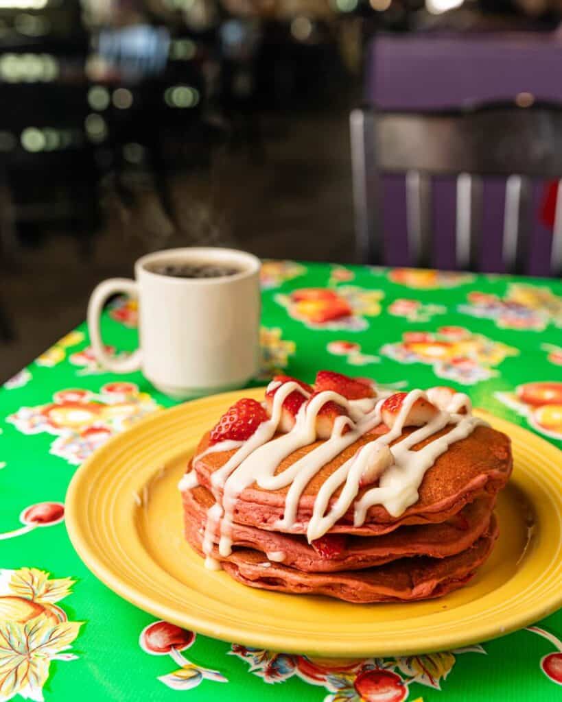 red velvet pancakes topped with strawberries and drizzled with sweet cream cheese, on a yellow plate
