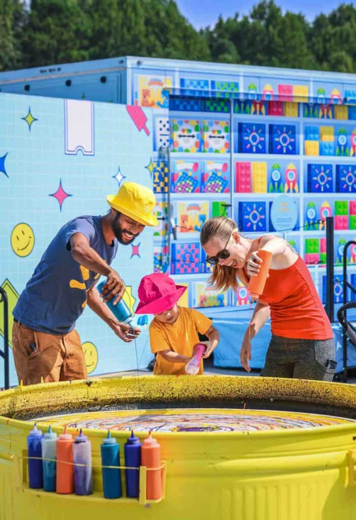 Two adults and a child adding paint to a large-scale spin-art project