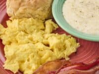 Photo of eggs, bacon, grits and biscuit on a red plate