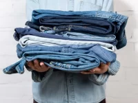 person wearing denim, holding pile of jeans