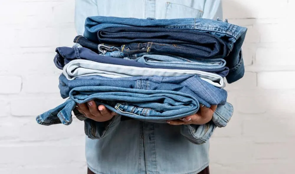 person wearing denim, holding pile of jeans