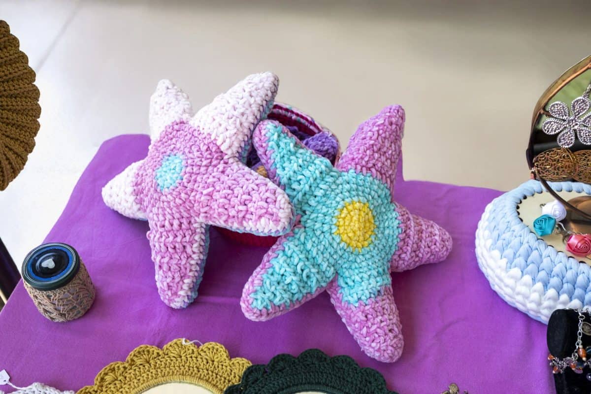 Colorful crocheted starfish toys are displayed on a purple surface at a craft market