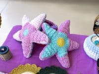 Colorful crocheted starfish toys are displayed on a purple surface at a craft market