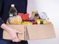 Woman volunteer hands holding food donations box with food grocery products.