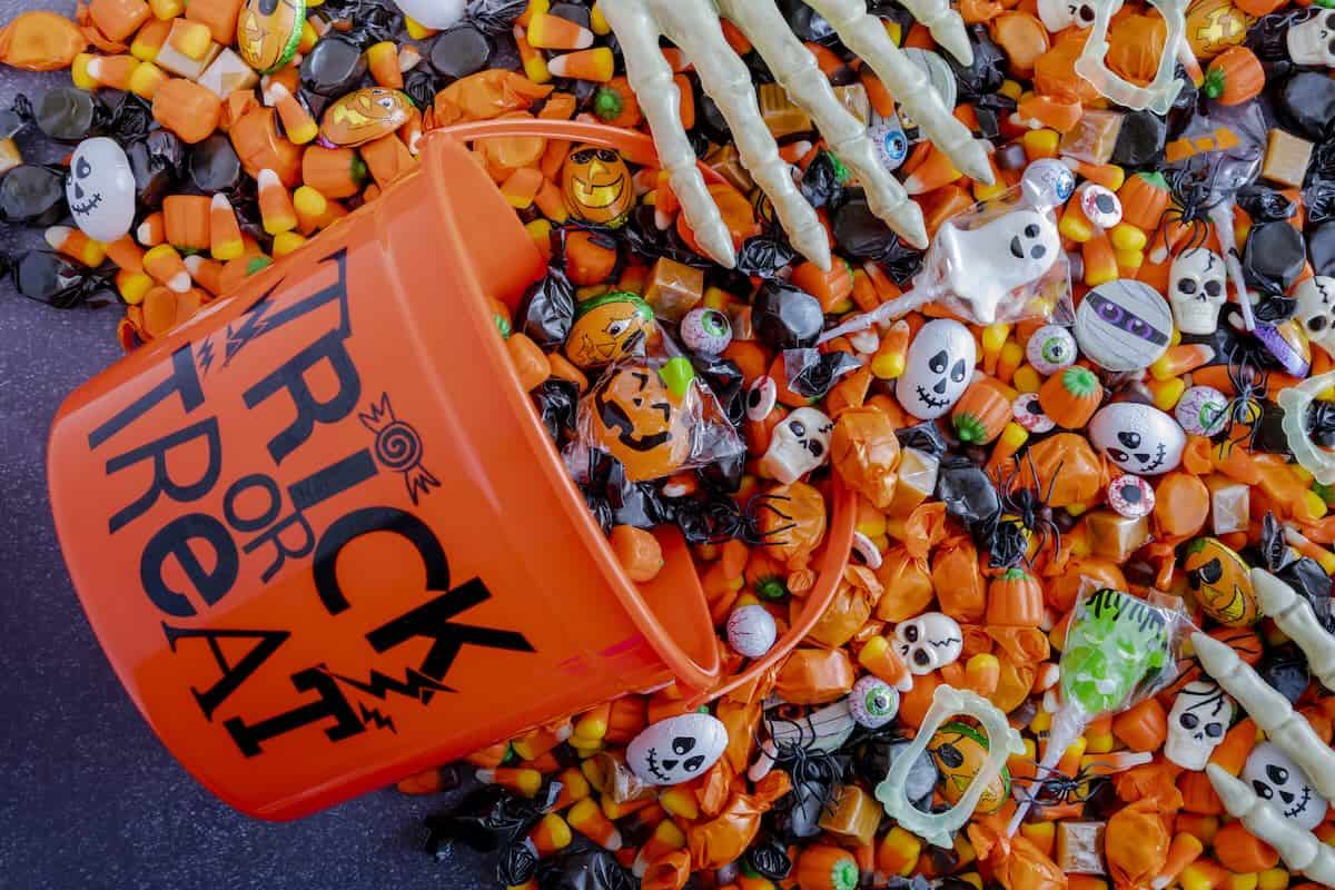trick or treat bucket with candy spilling out and a skeleton hand