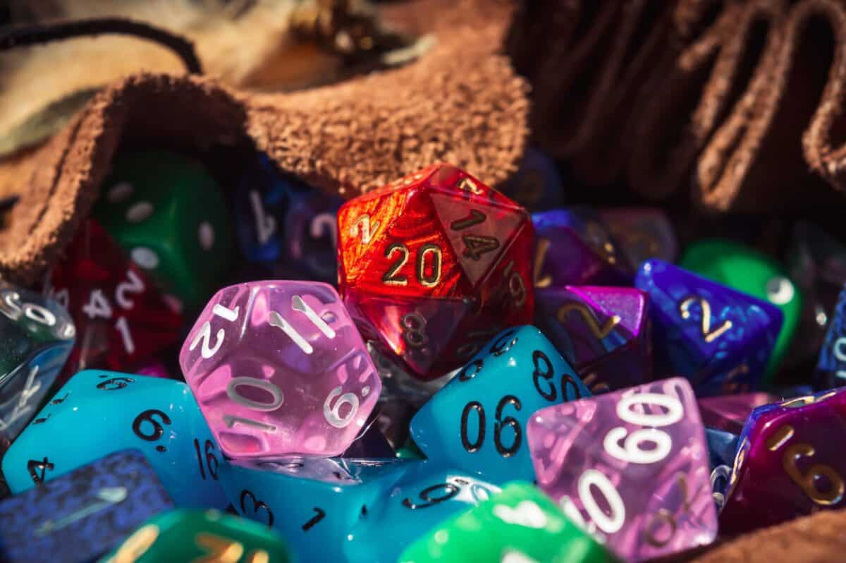 Close-up image of a red marbled 20-sided die on a pile of various colored and shaped dice spilling out of a dice bag in the warm sunlight