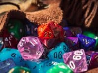 Close-up image of a red marbled 20-sided die on a pile of various colored and shaped dice spilling out of a dice bag in the warm sunlight