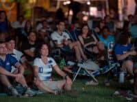People seated on a lawn watching a soccer game