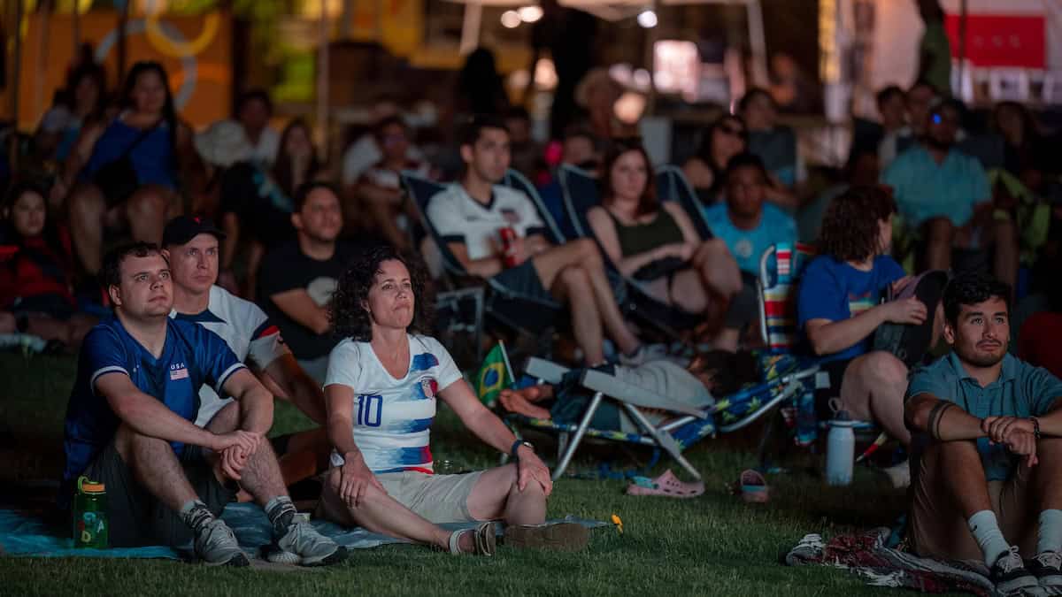 People seated on a lawn watching a soccer game